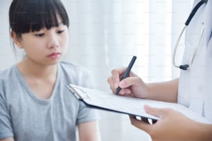 Medico femminile asiatico che prende nota sulla carta della lista di controllo per una bambina pazienti.