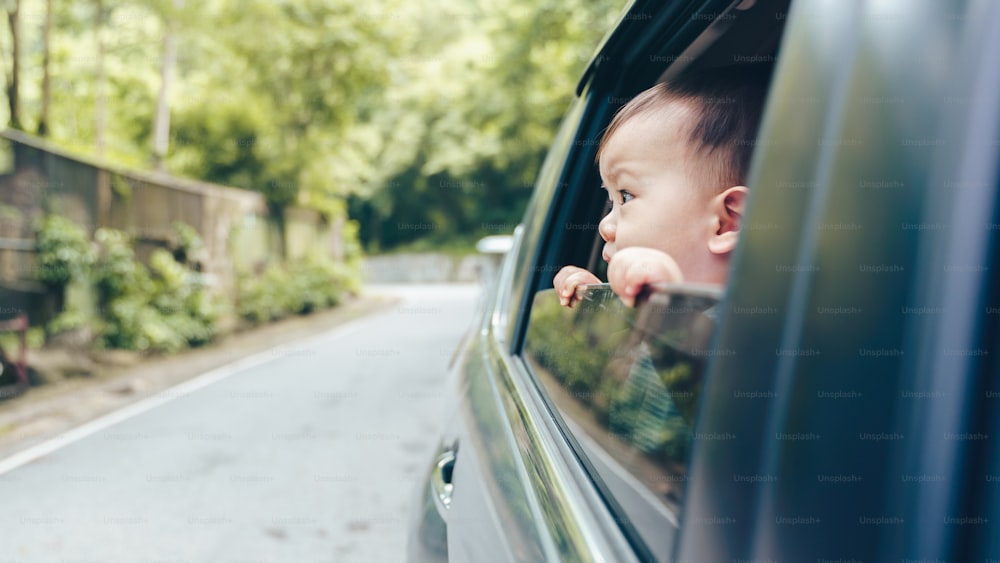 Piccolo ragazzo asiatico del bambino che guarda fuori dal finestrino dell'automobile mentre il viaggio in automobile, il viaggio su strada, le vacanze estive
