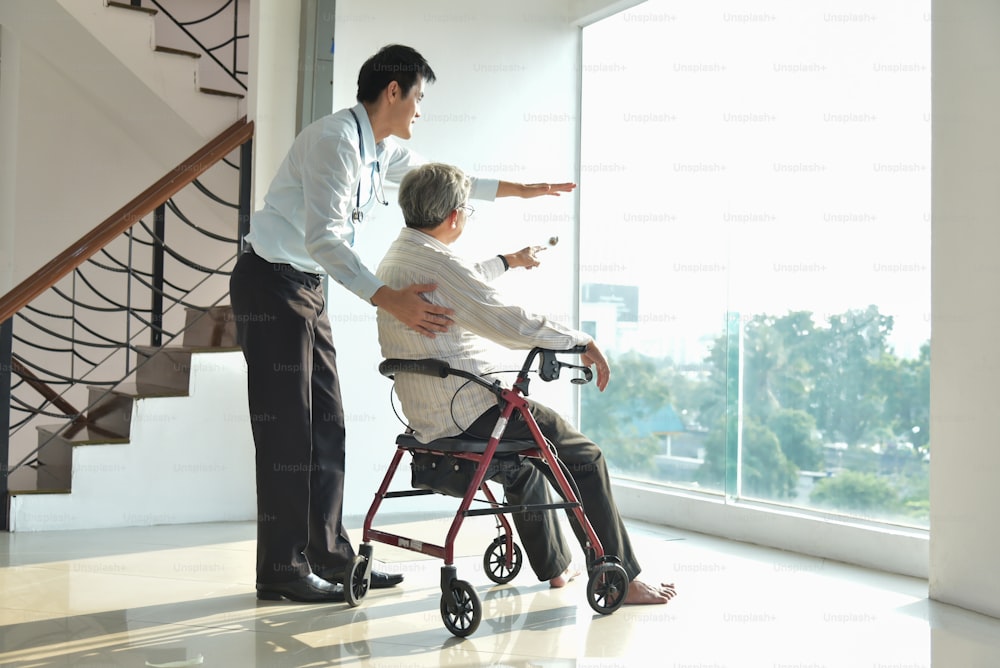 Asian Man Doctor is talking with his Senior male patient in a medical room. Elderly male sitting on wheelchair.  Health care, Paralysis, caregiver, consultant.