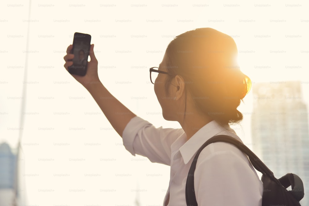 Femme chinoise prenant des selfies photo avec son téléphone intelligent sur l’arrière-plan d’un gratte-ciel dans la ville.