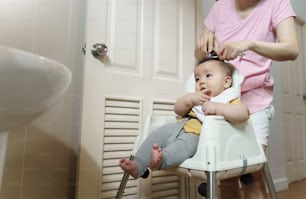 Petit bébé asiatique ayant une coupe de cheveux avec sa mère dans la salle de bain à la maison.