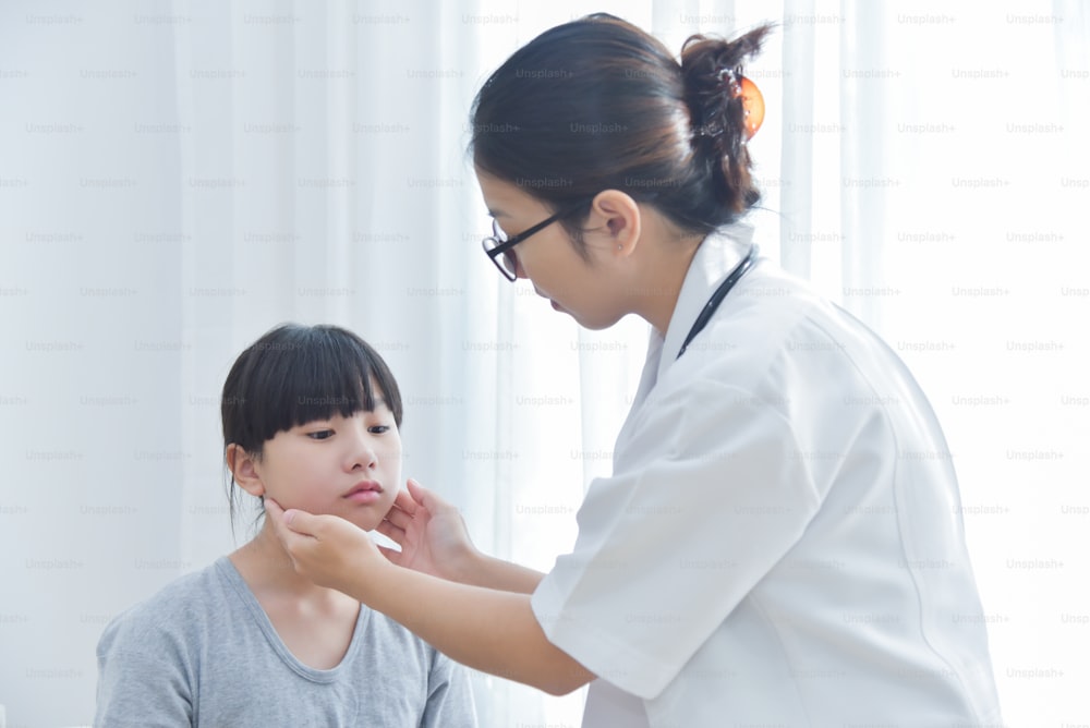 Jovem Médica Asiática examinando uma menina. Conceito de medicina e saúde. Ter dor no pescoço, dor na bochecha. Enxaqueca.