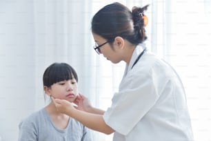Young Asian Female Doctor examining a little girl. Medicine and health care concept. Having neck pain, Cheek pain. Migraine.