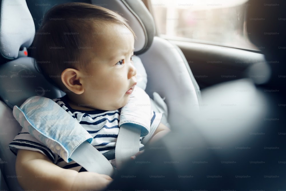 Heureux bébé garçon asiatique dans le siège auto, petit enfant en bas âge voyage en voiture avec la famille.