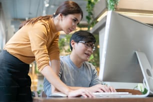Young Designers consulting and working on computer monitor together. Asian Businessman and businesswoman discussing and consulting business job in meeting at office