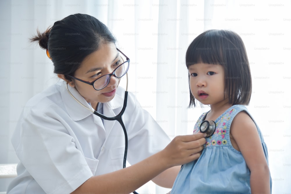 Junge asiatische Ärztin untersucht ein kleines Mädchen mit Stethoskop. Medizin und Gesundheitskonzept.
