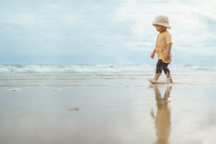 Chico asiático caminando por la playa. Niño adorable en vacaciones de verano al aire libre