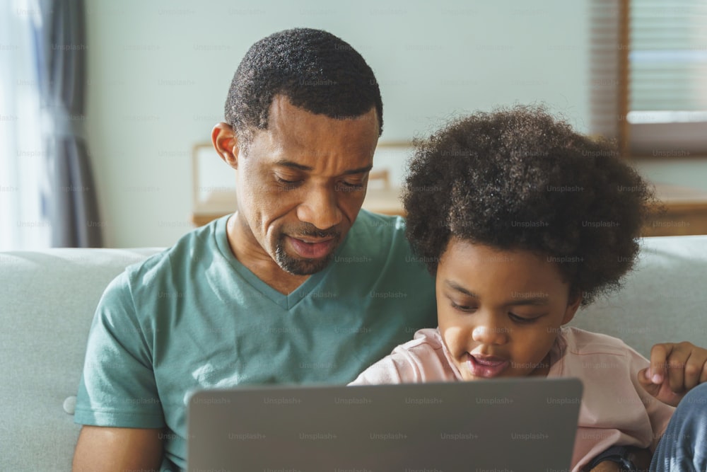 Smiling African American father and his cute son using laptop together.