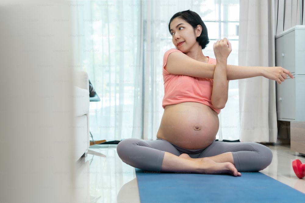 Jolie femme enceinte asiatique qui s’étire avant l’exercice de yoga à la maison.