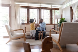 Afroamerikanischer Vater, der mit seinem kleinen Sohn auf der Couch des Wohnzimmers zu Hause spielt und Spaß hat. Glückliche schwarze Familie. Alleinerziehender