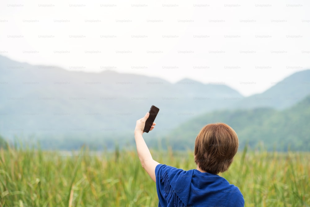 Mujer asiática feliz tomando una selfie con un teléfono inteligente en el campo y la vista de la montaña.