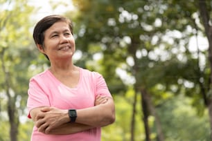Portrait of a smiling Asian senior woman with arms crossed in a park.