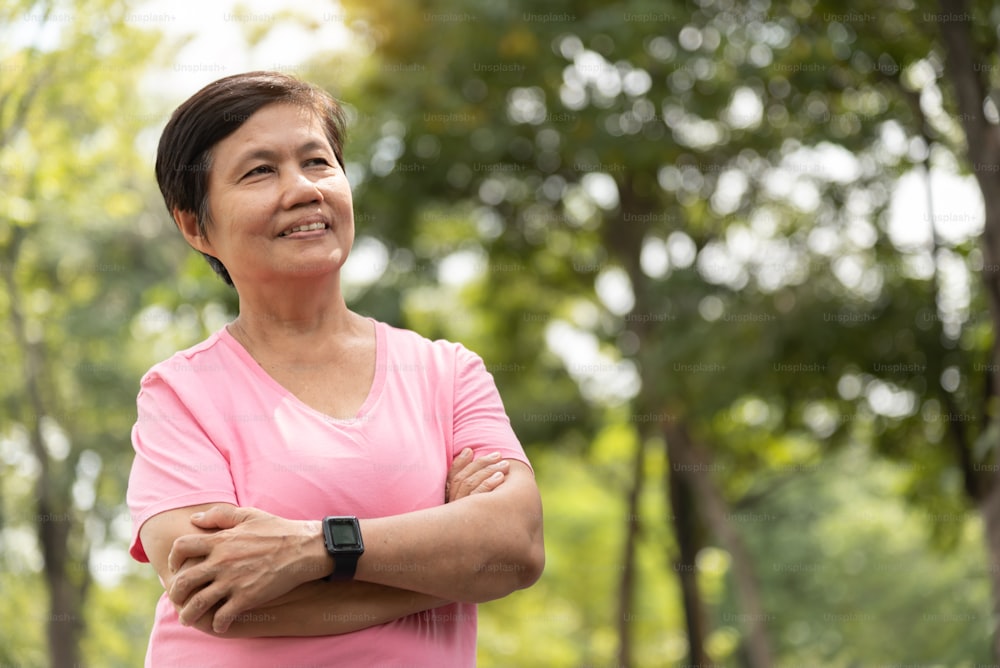 Portrait of a smiling Asian senior woman with arms crossed in a park.