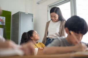 Jovem Professora Asiática ensinando sua menina afro-americana em sala de aula. Diversos estudantes multiétnicos crianças na escola internacional.
