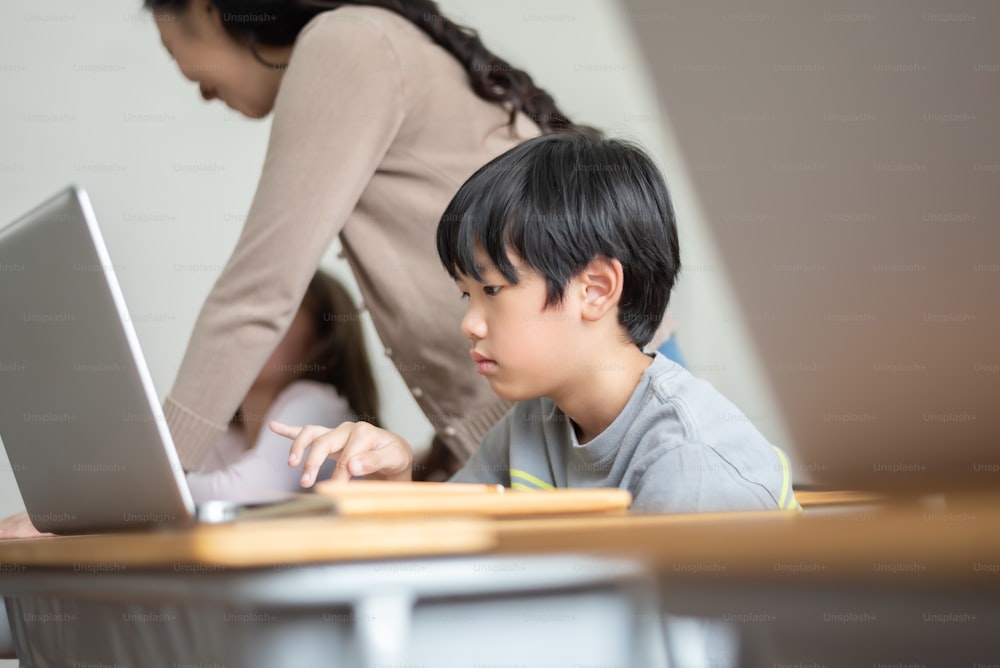 Niño japonés que estudia en una computadora portátil en una escuela primaria internacional.