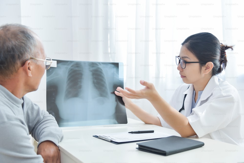 Junge asiatische Ärztin trägt eine Brille, die den Röntgenfilm eines älteren männlichen Patienten untersucht.