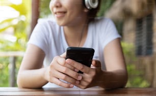 Glückliche asiatische Frau, die die Musik mit Kopfhörer und Smartphone im Freien hört. Spaß. Entspannt.