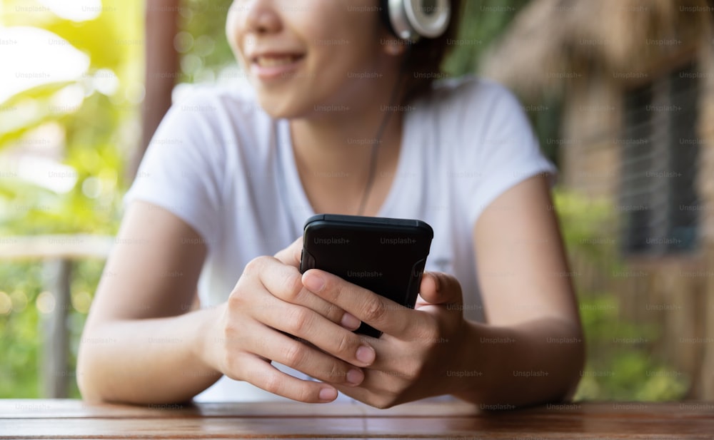 Femme asiatique heureuse écoutant la musique avec un casque et un téléphone intelligent à l’extérieur. S’amuser. Détendu.