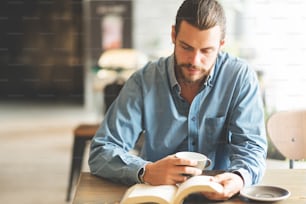 Freelancer masculino barbudo de camisa azul lendo um livro no café.