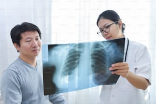 Young Asian female doctor wear glasses examining x-ray film of male patient.