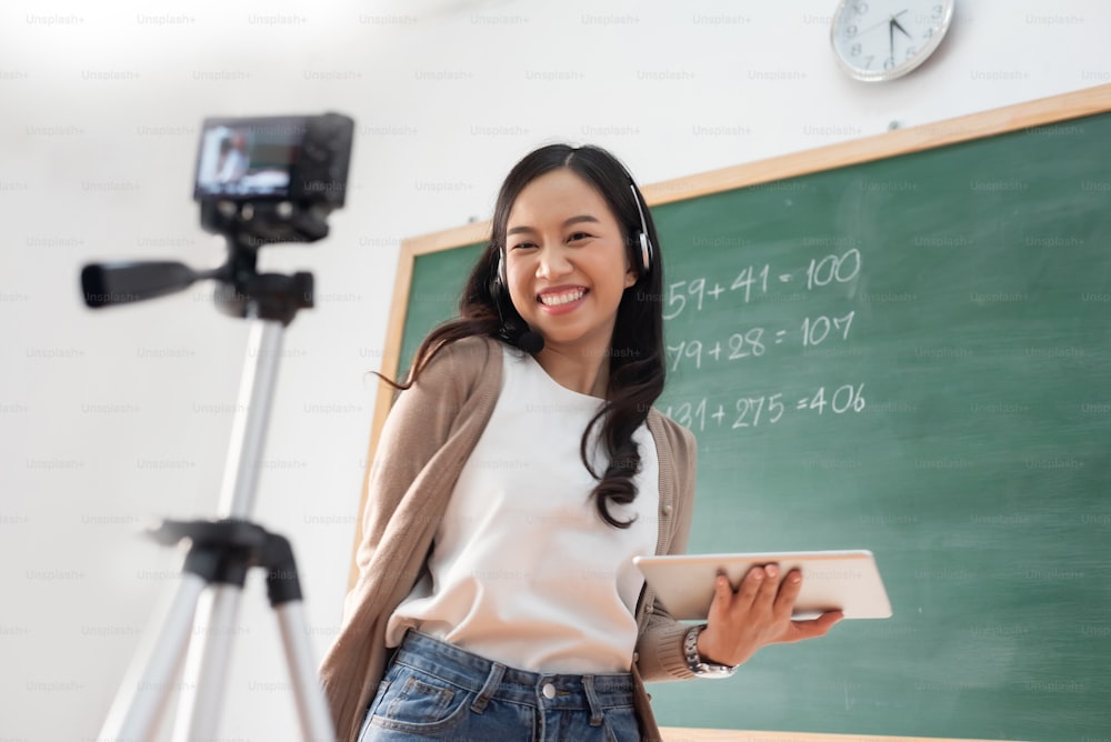 행복한 미소 예쁜 아시아 여자 선생님은 카메라와 디지털 태블릿, 화상 통화, 교실에서 튜토리얼에 대한 온라인 교육을 하고 있습니다.