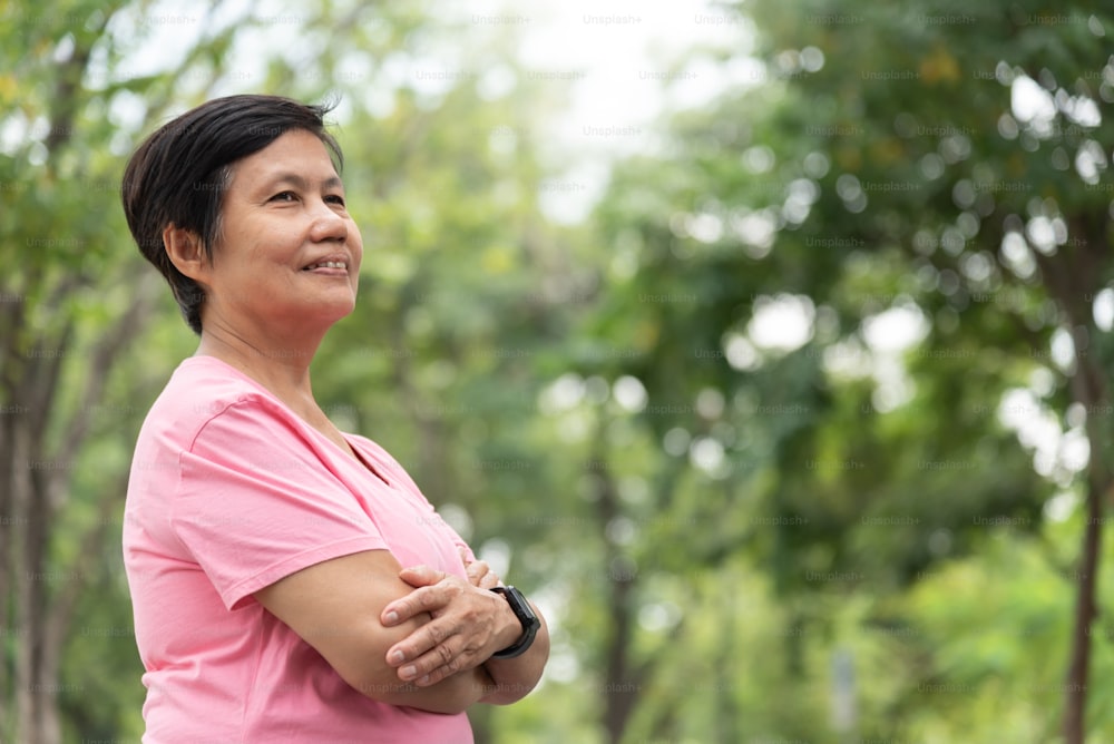 Portrait d’une femme adulte mature asiatique confiante avec les bras croisés dans un parc en plein air.