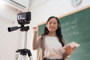Selective focus, Smiling Asian Young woman teacher teaching and recording video with digital camera at front of blackboard. Live stream.