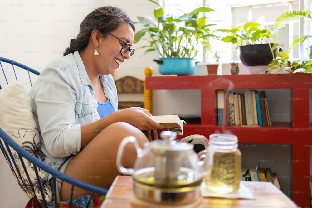 Mexikanische tätowierte Millennial-Frau, die ein Buch im Wohnzimmer liest