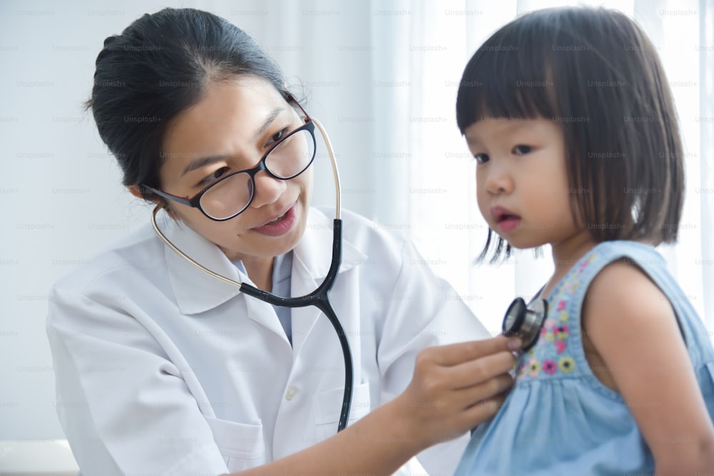 Joven doctora asiática examinando a una niña con estetoscopio. Concepto de medicina y cuidado de la salud.