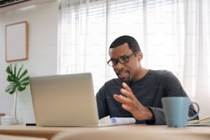Hombre afroamericano teniendo videoconferencia con un colega en casa. Freelancer masculino africano negro usando una computadora portátil en una reunión en línea.