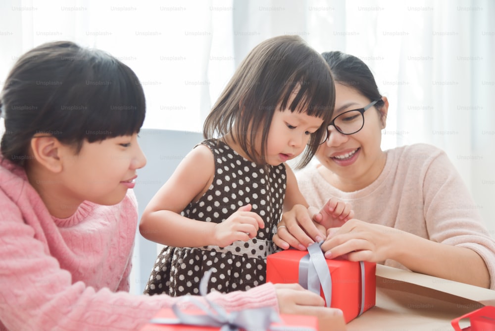 Família asiática feliz embrulhando uma caixa de presente vermelha para aniversário, Natal e Ano Novo em uma sala branca na casa.