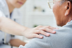 Close up on hand. Young Asian Female doctor comforting senior male patient in medical office.