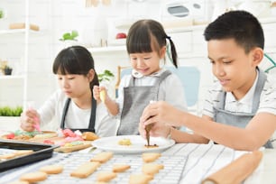 Asian Kids decorating cookies in the kitchen.