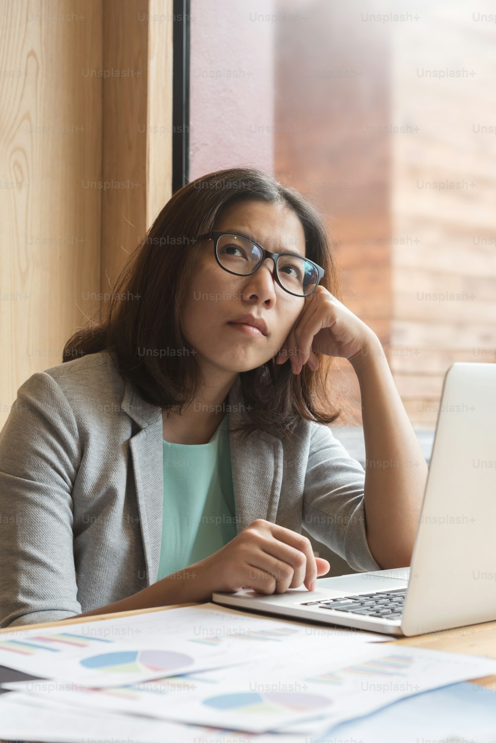 Mulher de negócios asiática com laptop pensando em seu trabalho em seu local de trabalho.
