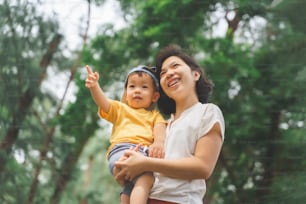 Alegre y sonriente madre asiática joven sosteniendo a su pequeño hijo en la naturaleza al aire libre