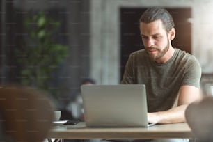 Designer dell'uomo barbuto che utilizza il computer portatile per effettuare la prenotazione online nel caffè. Libero professionista hipster che lavora in un ristorante
