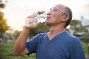 公園の屋外背景で運動した後のアジアの年配の男性の飲料水。