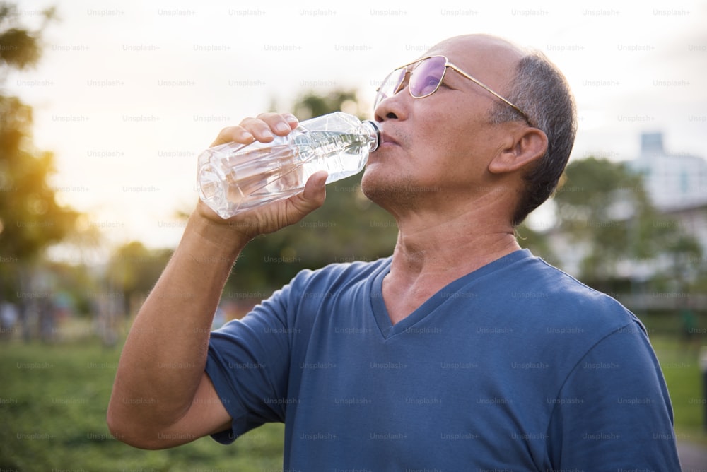 Asiatique senior masculin boire de l’eau après l’exercice au fond extérieur du parc.