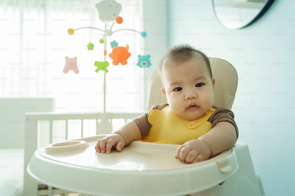 Portrait of Asian little cute baby boy sitting in high chair while waiting for his Mother feeding food