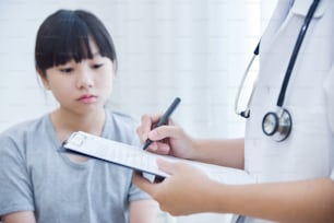 Asiatische Ärztin notiert sich auf Checklistenpapier für kleine Mädchenpatienten.