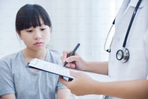 Asian Female Doctor taking note on checklist paper for a little girl patients.