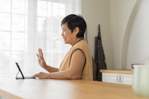 Glückliche asiatische ältere Frau mit Blick auf digitalen Tablet-Computer, Online-Videoanruf mit Familie.