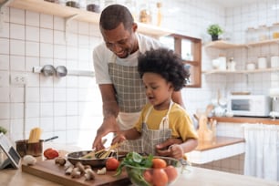 Padre afroamericano negro enseñando a su hijo afro a cocinar en la cocina de su casa