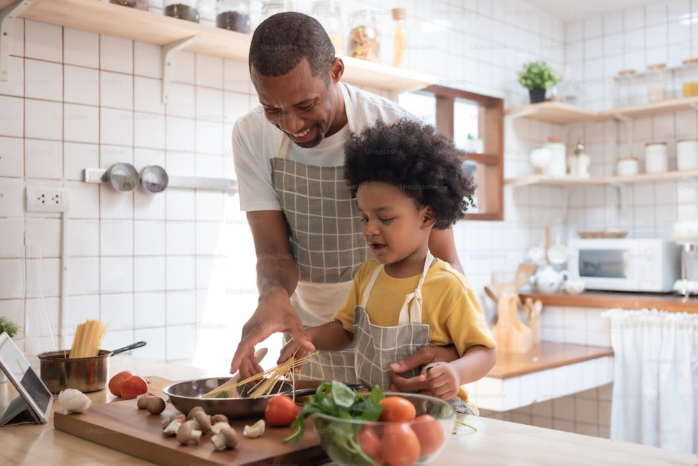 Pai afro-americano negro ensinando seu filho afro cozinhando na cozinha em casa