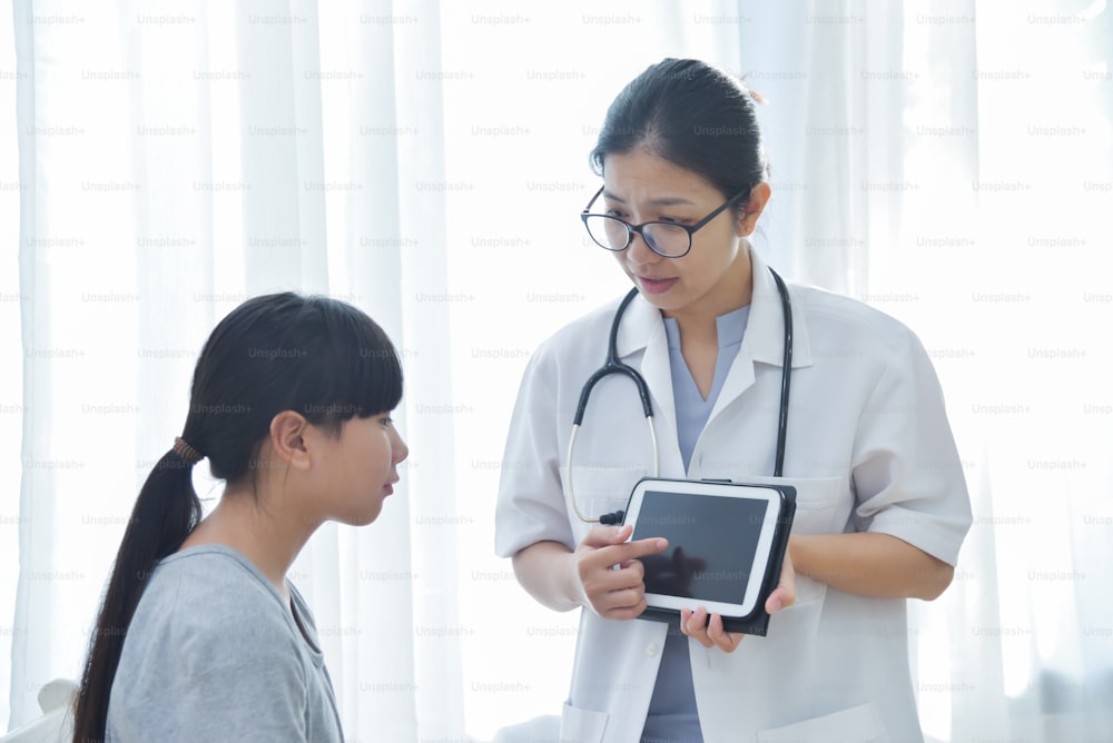 젊은 아시아 여성 의사가 디지털 태블릿 컴퓨터를 들고 어린 소녀를 검사하고 있다. 의학 및 건강 관리 개념입니다.