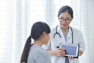 Jovem Médica Asiática segurando o computador tablet digital e examinando uma menina. Conceito de medicina e saúde.