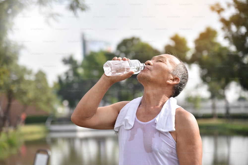 Asiatischer älterer Mann trinkt Wasser nach dem Training im Park im Freien.