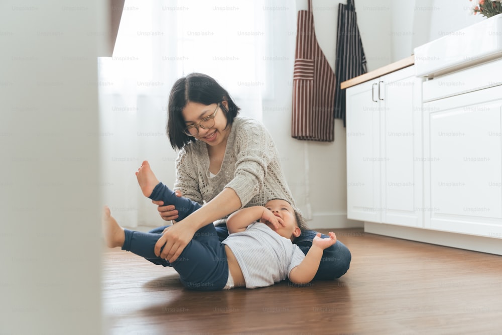 Chinese mother playing with little cute toddler boy on floor at home, Happy Asian Family having Fun in kitchen indoors.