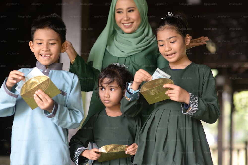 イスラム教徒の家族、子供たちは祝福としてお金の包みを受け取りました、ハリラヤイードアルフィトルのコンセプト。