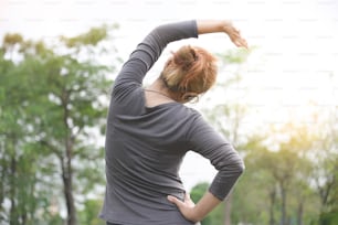 Asian female workout at the park. Young woman is warming up and stretching her arms at outdoors on morning. Health care and sport concept. Rear view. Exercising.